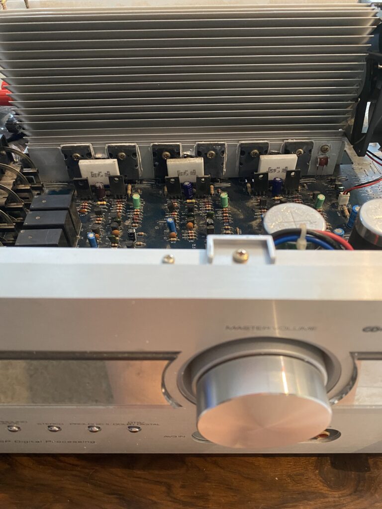 Otwarty amplituner marki KODA z widoczną elektroniką na stole warsztatowym po wymianie około stu kondensatorów przez serwisanta.