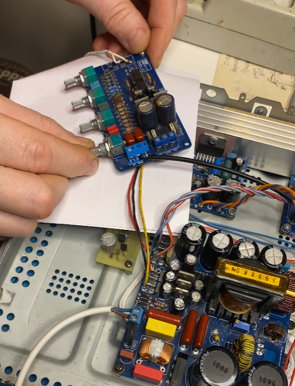 Elektronik trzymający w dłoniach płytkę drukowaną wzmacniacza bez obudowy, kręcący potencjometrami w celu kalibracji i konfiguracji dźwięku.